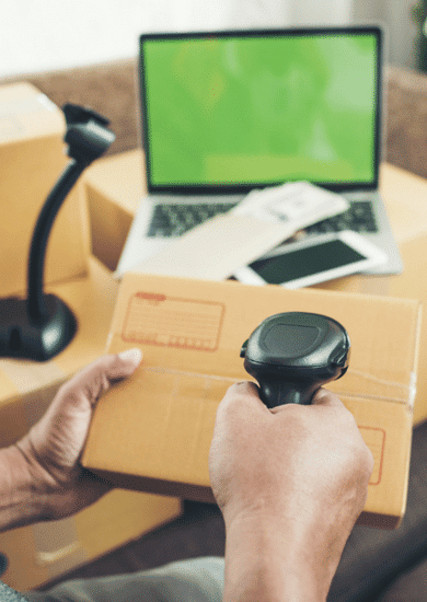 A person scans a brown courier package with a barcode scanner, likely for package entry related to international shipping or e-commerce logistics.
